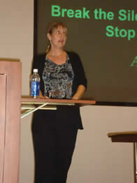 A woman at a pdoium giving a presentation on stopping violence on women.