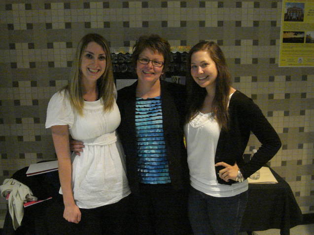 Two smiling students being hugged by their professor.