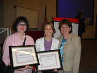 Two students holding certificates while another woman hugs them.
