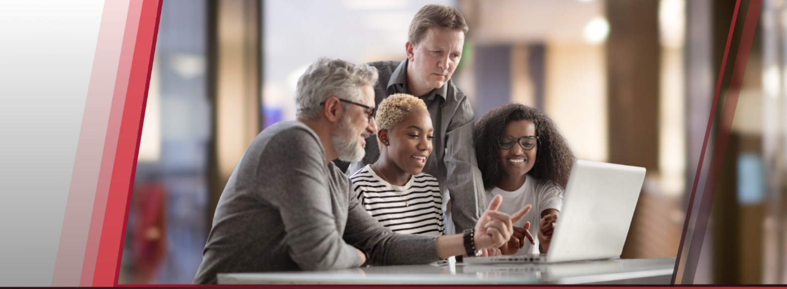 Four coworkers gathered around a laptop, smiling and discussing something on the screen in a modern office.