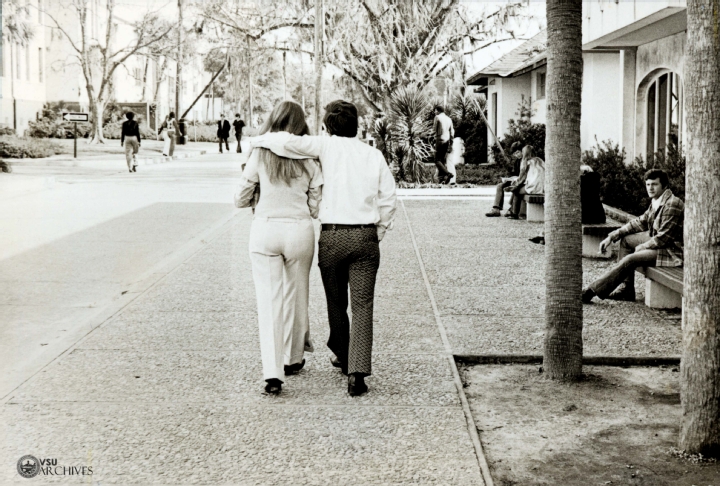 A couple walk down the sidewalk in front of the old Student Union, circa 1970