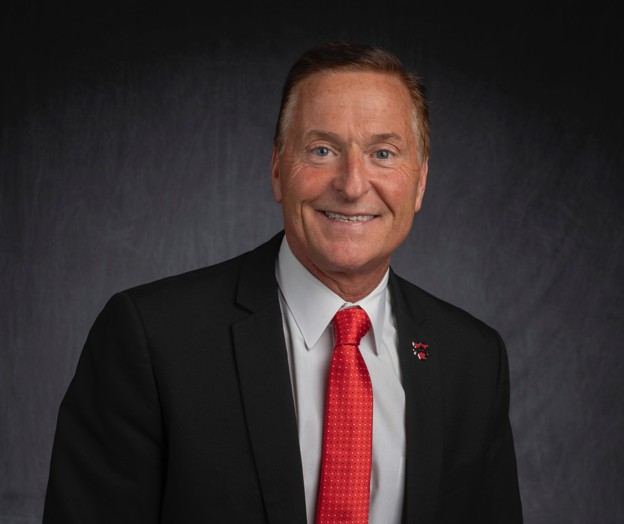 Studio headshot of a President Don Green in a black suit and white shirt with a red tie, against a dark gray backdrop.