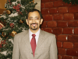 A man in a tan suit standing in front of a Christmas tree.