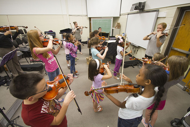 boys and girls in music classroom with their teacher learning to play violin.